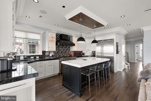 kitchen featuring wall chimney range hood, premium appliances, a sink, and visible vents