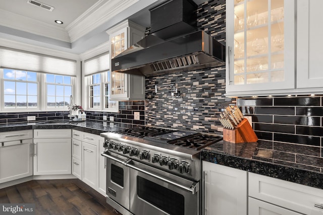 kitchen with visible vents, range with two ovens, glass insert cabinets, crown molding, and wall chimney range hood