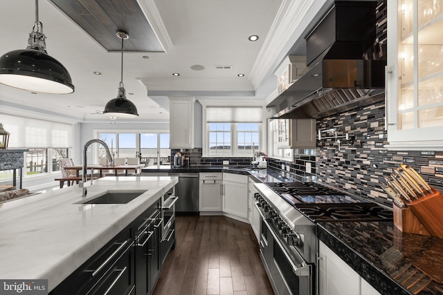 kitchen featuring white cabinets, appliances with stainless steel finishes, ornamental molding, wall chimney range hood, and a sink