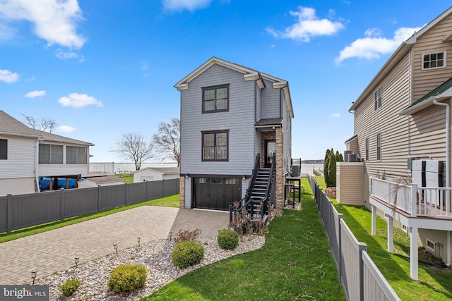 rear view of property with stairs, a lawn, fence, and decorative driveway