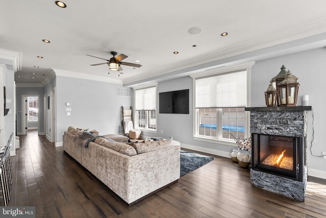 living area with baseboards, a stone fireplace, dark wood-type flooring, and crown molding