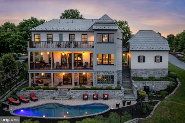 back of property at dusk featuring a balcony, a high end roof, a fenced in pool, and a patio