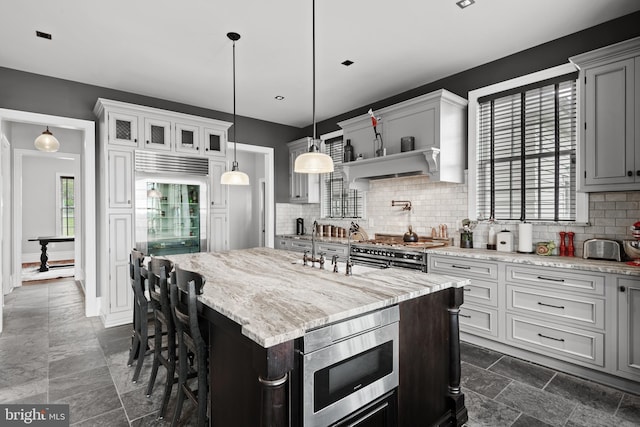 kitchen with glass insert cabinets, a breakfast bar area, hanging light fixtures, a kitchen island with sink, and stainless steel appliances