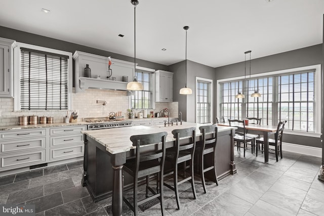 kitchen featuring a kitchen breakfast bar, a center island with sink, light stone countertops, tasteful backsplash, and decorative light fixtures