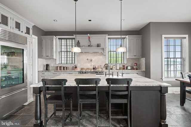 kitchen featuring glass insert cabinets, pendant lighting, a kitchen island with sink, and a breakfast bar area