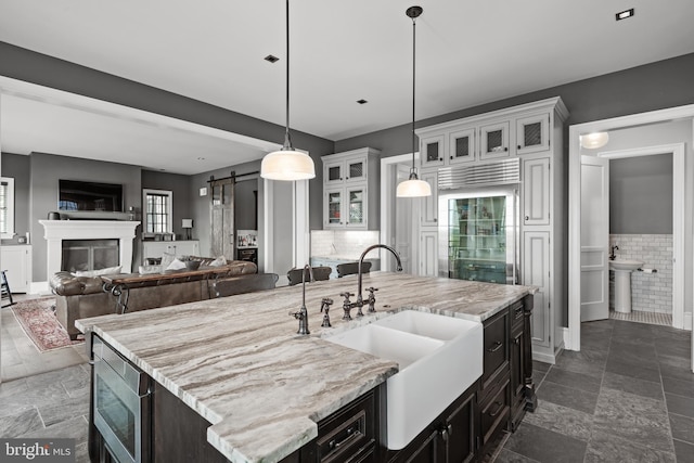 kitchen featuring a barn door, white cabinets, an island with sink, glass insert cabinets, and a sink