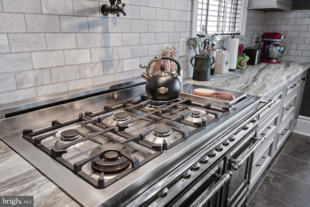 kitchen featuring cooktop, range with two ovens, light stone counters, and decorative backsplash