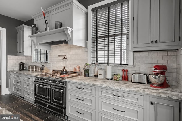 kitchen with tasteful backsplash, range with two ovens, dark wood-style floors, light stone countertops, and premium range hood