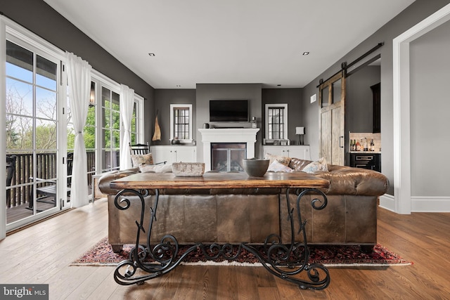 living area with light wood-style floors, a barn door, baseboards, and a glass covered fireplace