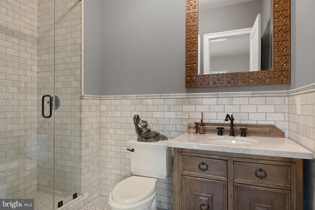 full bath with wainscoting, toilet, vanity, a shower stall, and tile walls