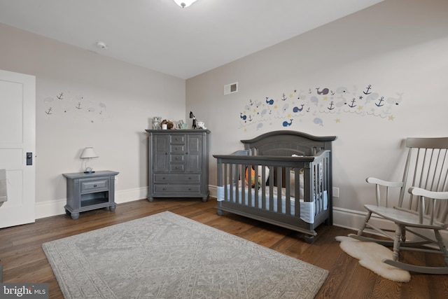 bedroom featuring a nursery area, dark wood-style flooring, visible vents, and baseboards