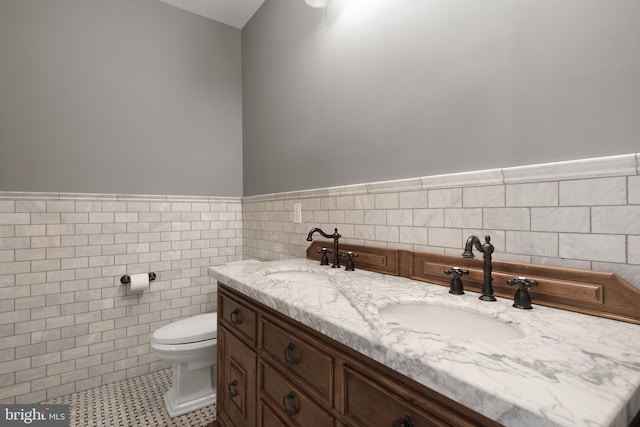 bathroom featuring a sink, tile walls, toilet, and double vanity