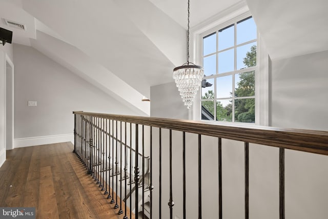 corridor with a notable chandelier, dark wood-type flooring, visible vents, baseboards, and vaulted ceiling