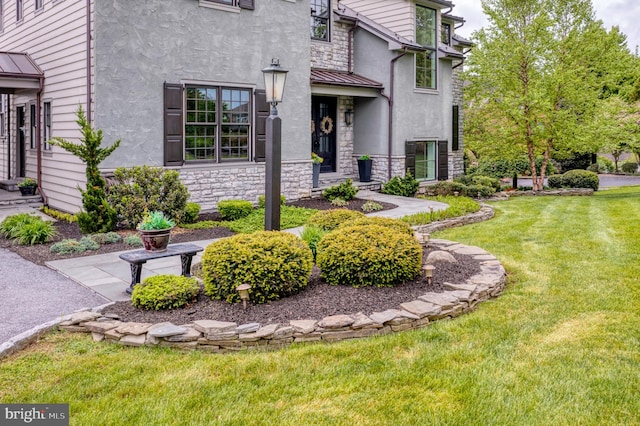 property entrance with a standing seam roof, stone siding, metal roof, and a lawn