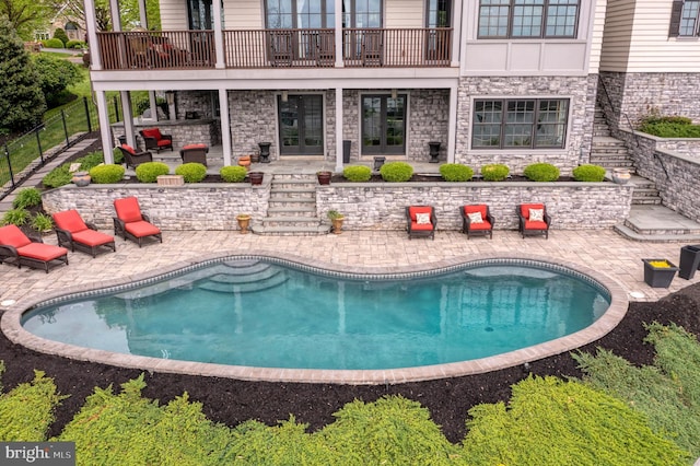 back of house with stone siding, an outdoor pool, and a patio