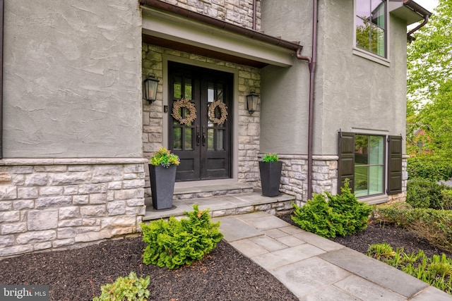 doorway to property with stone siding, french doors, and stucco siding