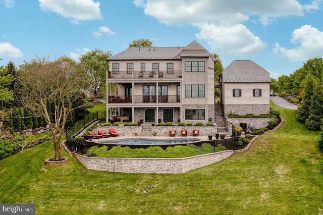 back of house featuring a balcony, stone siding, and a lawn