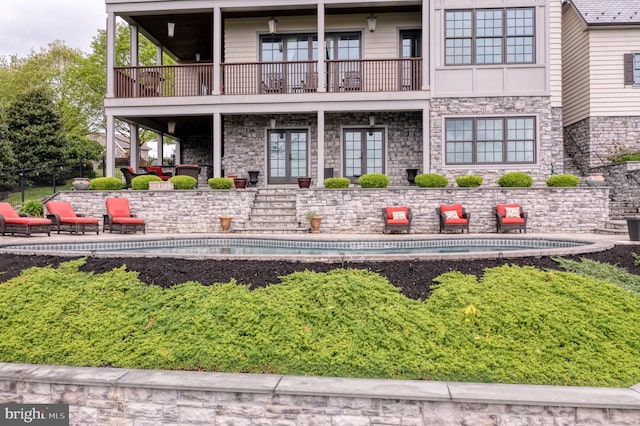 back of property with stone siding, a patio area, and a balcony