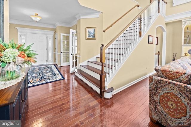 entrance foyer featuring arched walkways, dark wood finished floors, crown molding, stairway, and baseboards