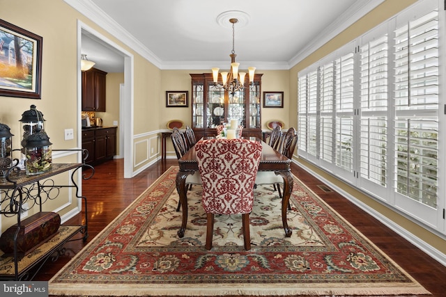 dining room featuring an inviting chandelier, dark wood finished floors, crown molding, and wainscoting