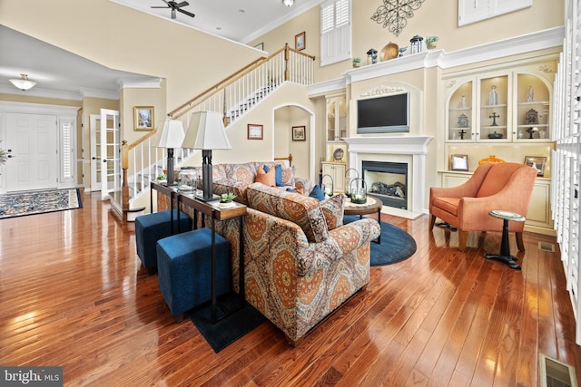 living room with a fireplace, a high ceiling, ornamental molding, hardwood / wood-style floors, and stairs