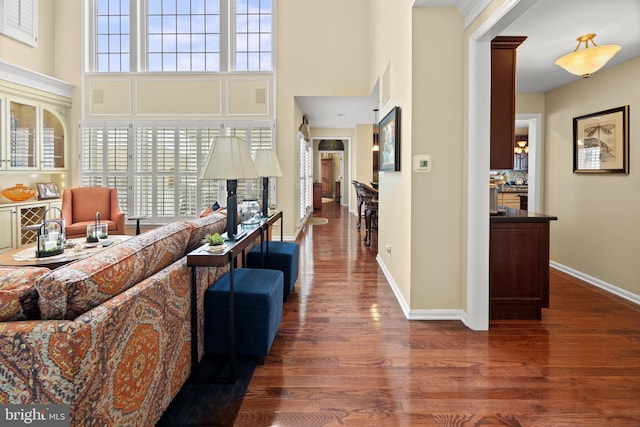 living room featuring wood finished floors, a towering ceiling, and baseboards