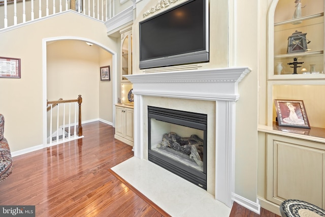 interior details with arched walkways, built in shelves, wood finished floors, a fireplace with flush hearth, and baseboards