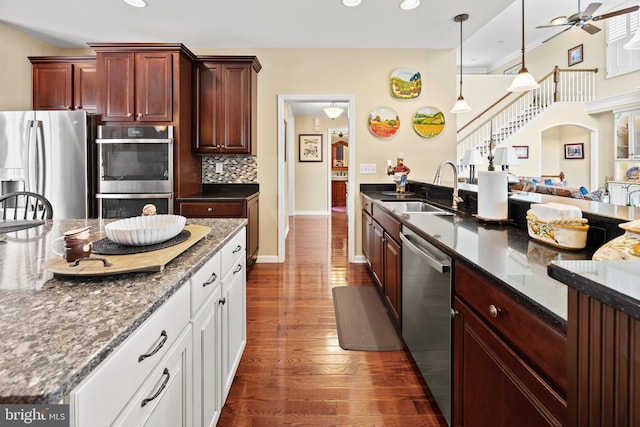 kitchen with ceiling fan, dark wood-style flooring, a sink, stainless steel appliances, and backsplash