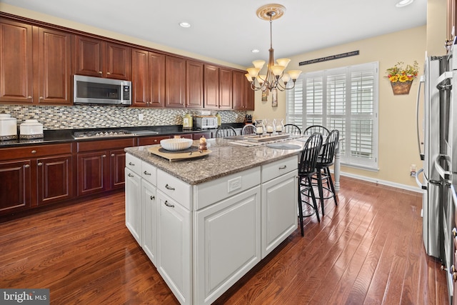 kitchen featuring dark wood finished floors, decorative backsplash, appliances with stainless steel finishes, a center island, and an inviting chandelier