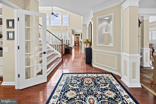 foyer featuring decorative columns, a decorative wall, stairway, ornamental molding, and wood finished floors