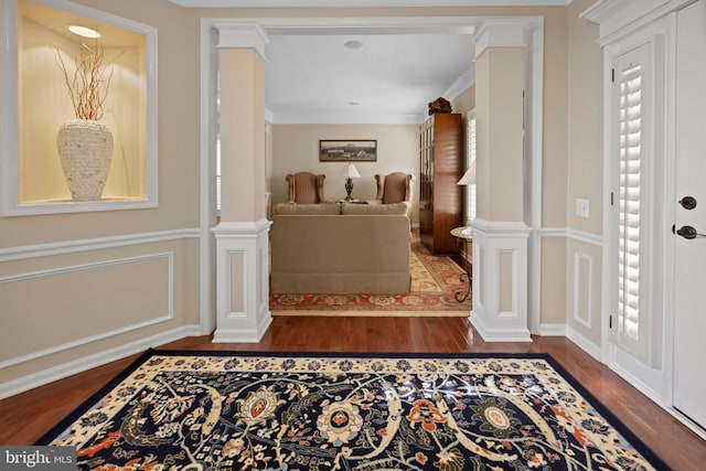 entrance foyer with crown molding, wood finished floors, decorative columns, and a decorative wall