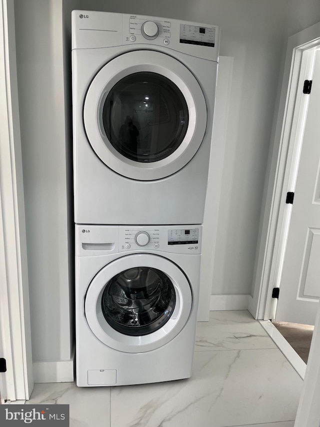 laundry room with stacked washer / drying machine, marble finish floor, baseboards, and laundry area