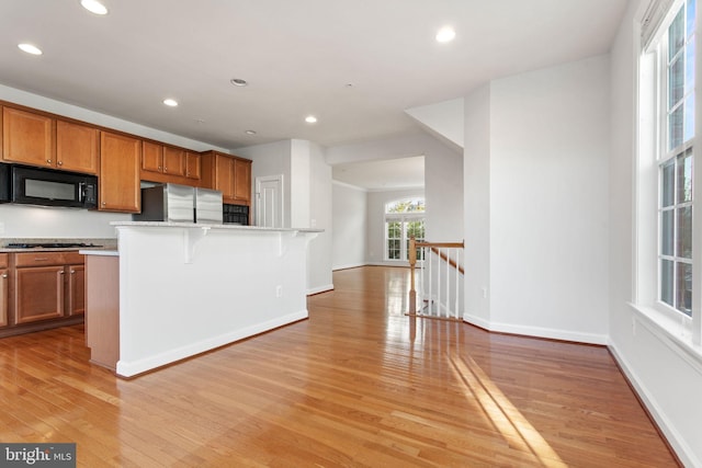 kitchen with brown cabinetry, a kitchen breakfast bar, freestanding refrigerator, a kitchen island with sink, and black microwave