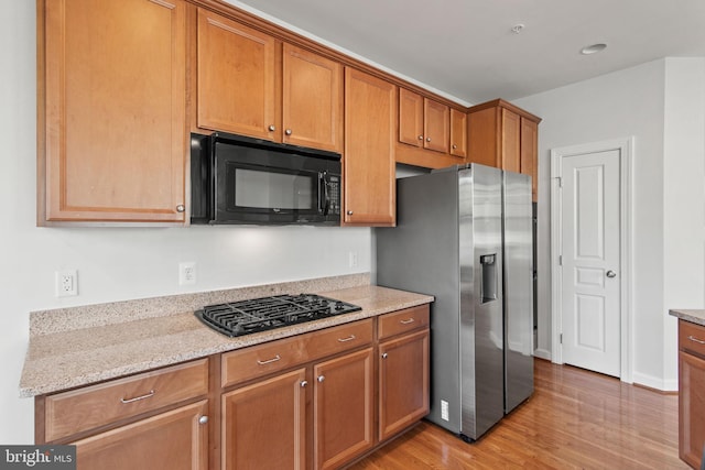 kitchen featuring light stone countertops, black appliances, light wood-type flooring, and brown cabinets