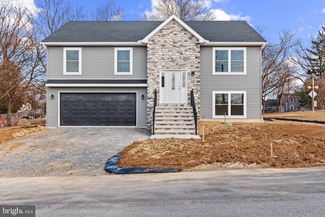 split foyer home featuring driveway, stone siding, roof with shingles, and an attached garage