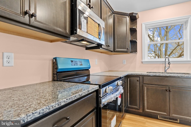 kitchen with stainless steel appliances, visible vents, light wood-style flooring, a sink, and dark brown cabinetry