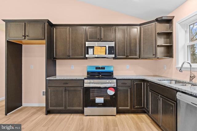 kitchen with light stone counters, open shelves, stainless steel appliances, a sink, and dark brown cabinetry