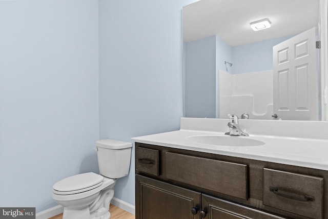 bathroom featuring baseboards, toilet, wood finished floors, walk in shower, and vanity