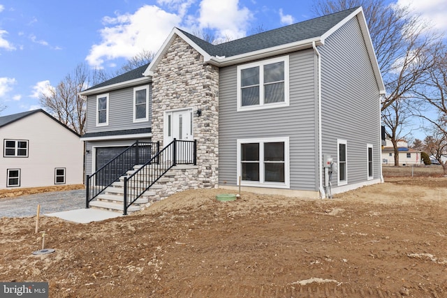 split foyer home featuring an attached garage, stone siding, and roof with shingles