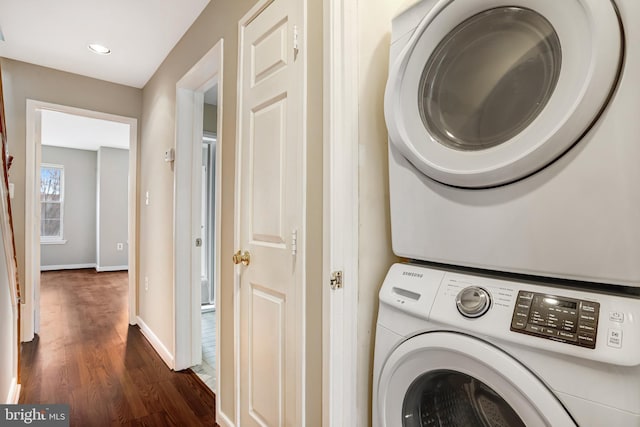 laundry room featuring laundry area, baseboards, dark wood finished floors, and stacked washer and clothes dryer