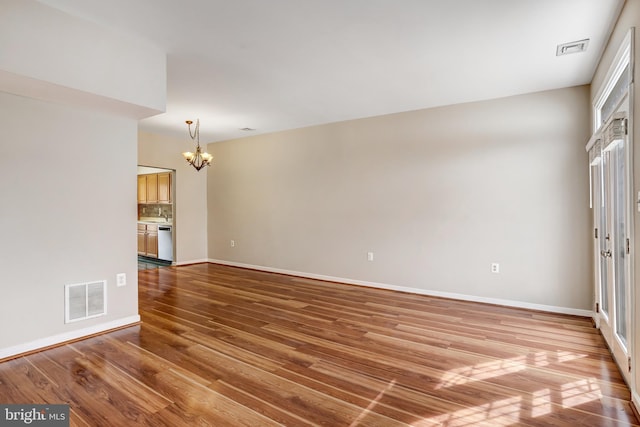 empty room featuring a chandelier, wood finished floors, visible vents, and baseboards