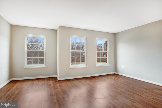 spare room featuring plenty of natural light, baseboards, and wood finished floors