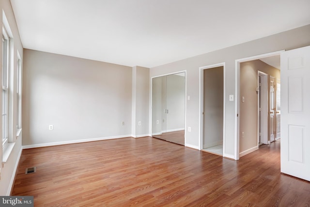 unfurnished bedroom featuring baseboards, multiple windows, visible vents, and wood finished floors