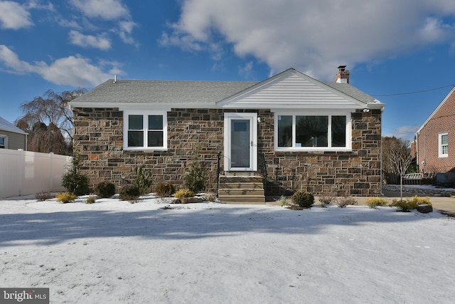 view of front of property featuring entry steps, stone siding, a chimney, and fence