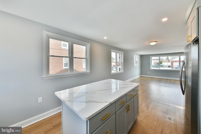 kitchen with gray cabinets, freestanding refrigerator, a kitchen island, light stone countertops, and light wood-type flooring