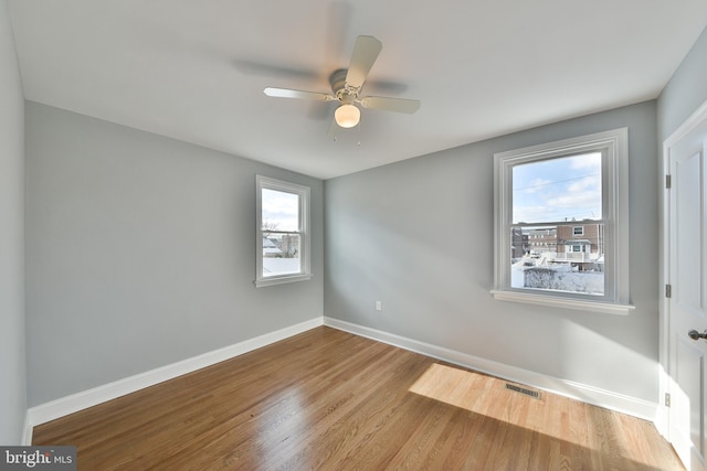 spare room featuring light wood-style floors, baseboards, visible vents, and a ceiling fan