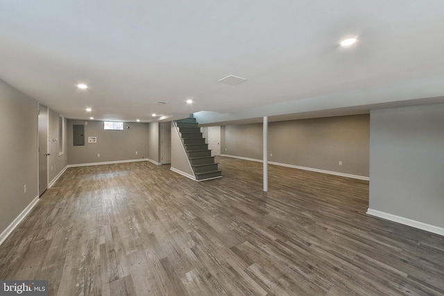 basement with dark wood finished floors, recessed lighting, stairway, electric panel, and baseboards