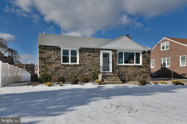 view of front of property featuring a shingled roof, stone siding, fence, and a chimney