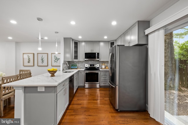 kitchen featuring light stone counters, gray cabinets, appliances with stainless steel finishes, a peninsula, and a sink