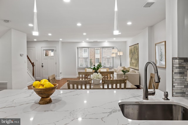 kitchen with a sink, visible vents, light stone counters, and open floor plan